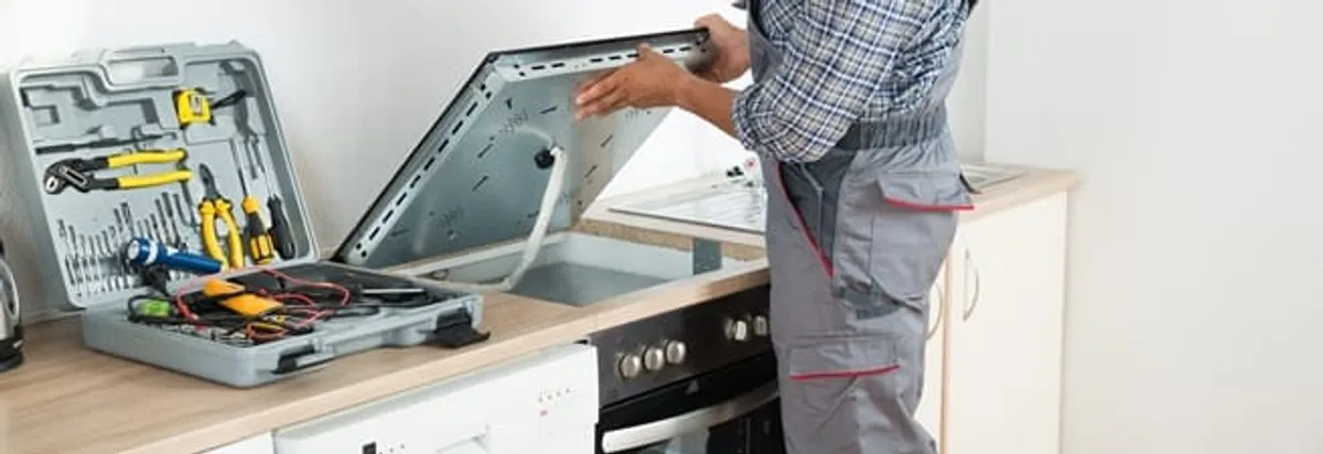Cooktop repair technician lifting a built-in stovetop for service in Lincoln, NE